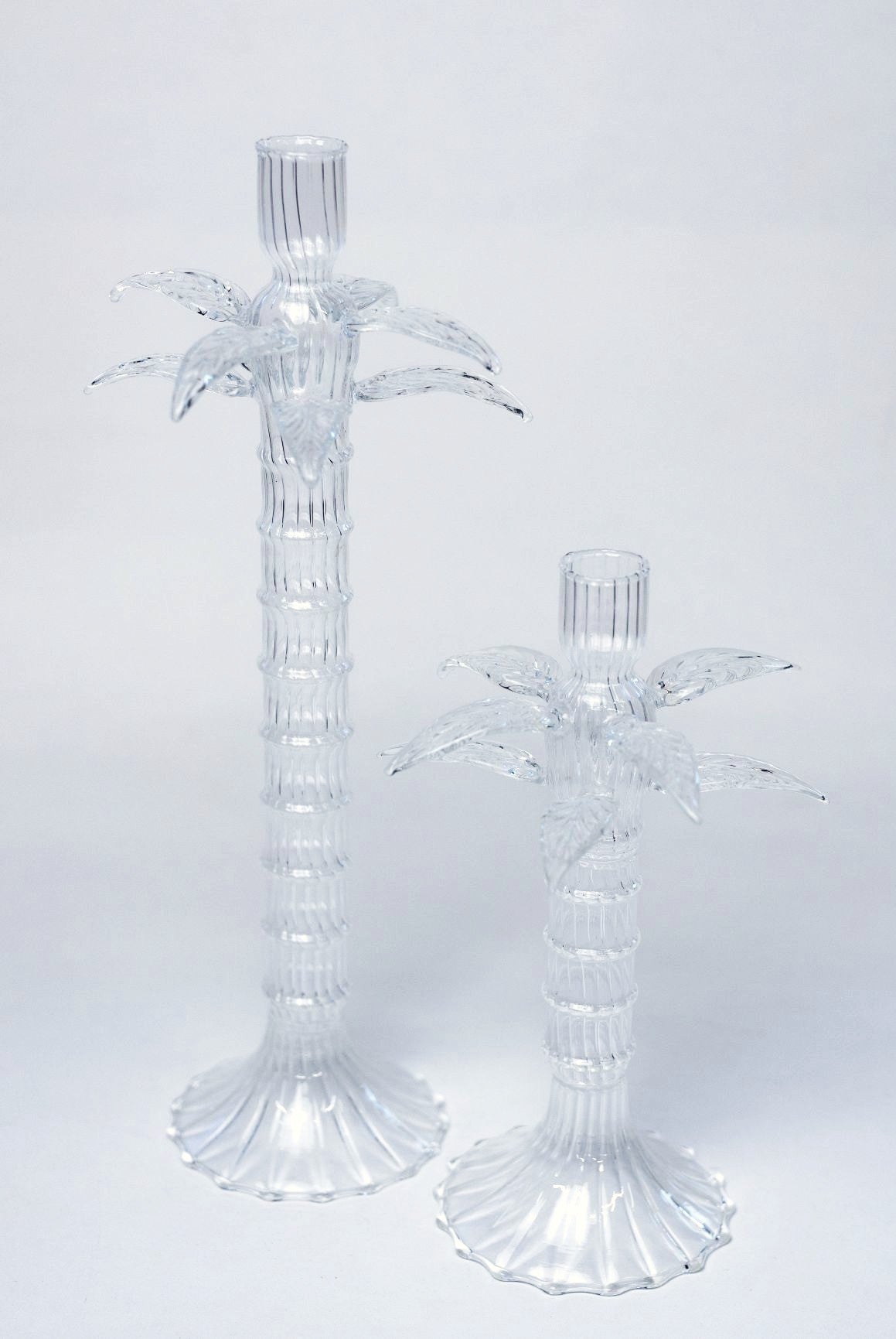 Two clear palm tree-shaped candle holders on a light gray background