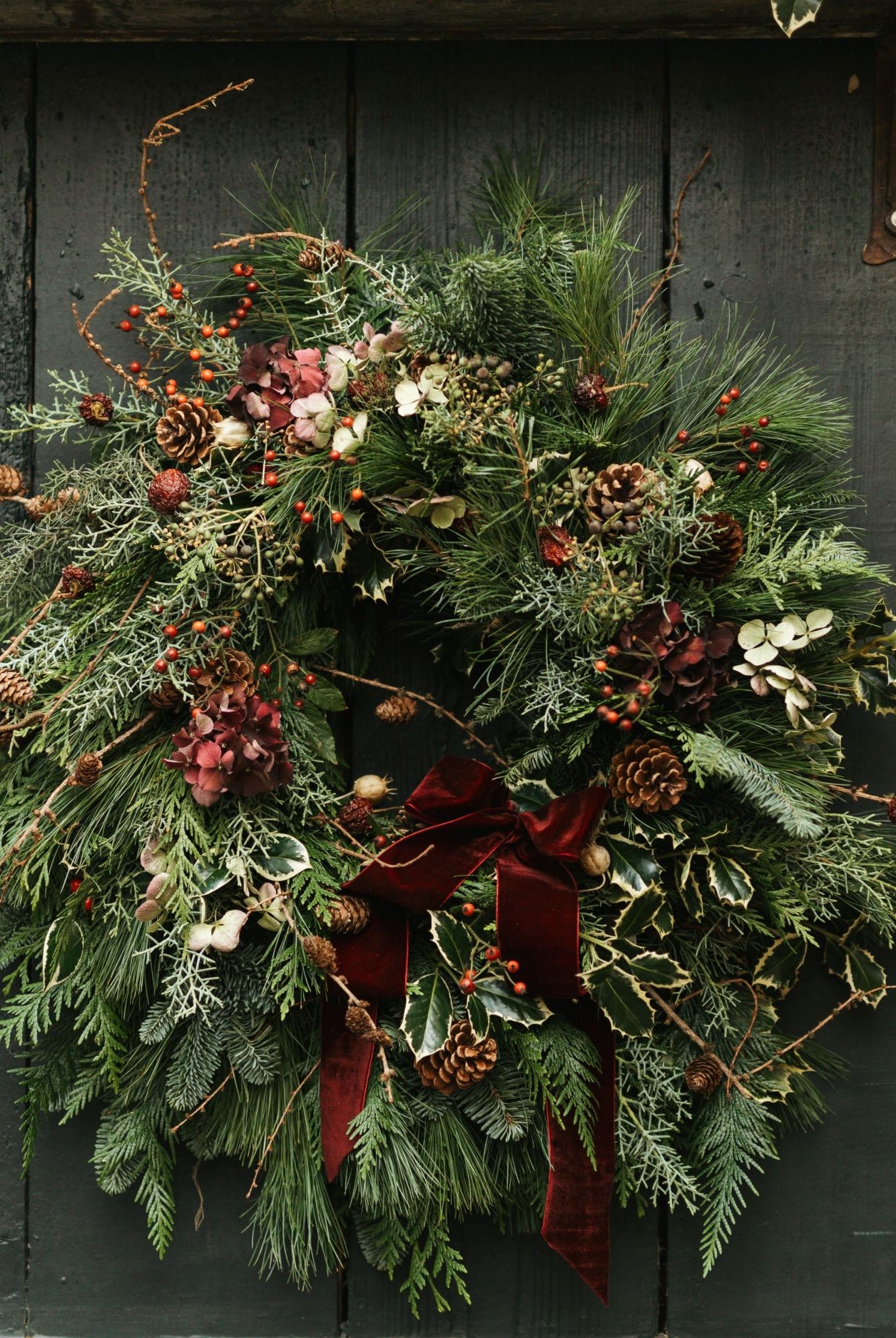Christmas wreath with greenery, berries, and a red ribbon on a dark wooden background