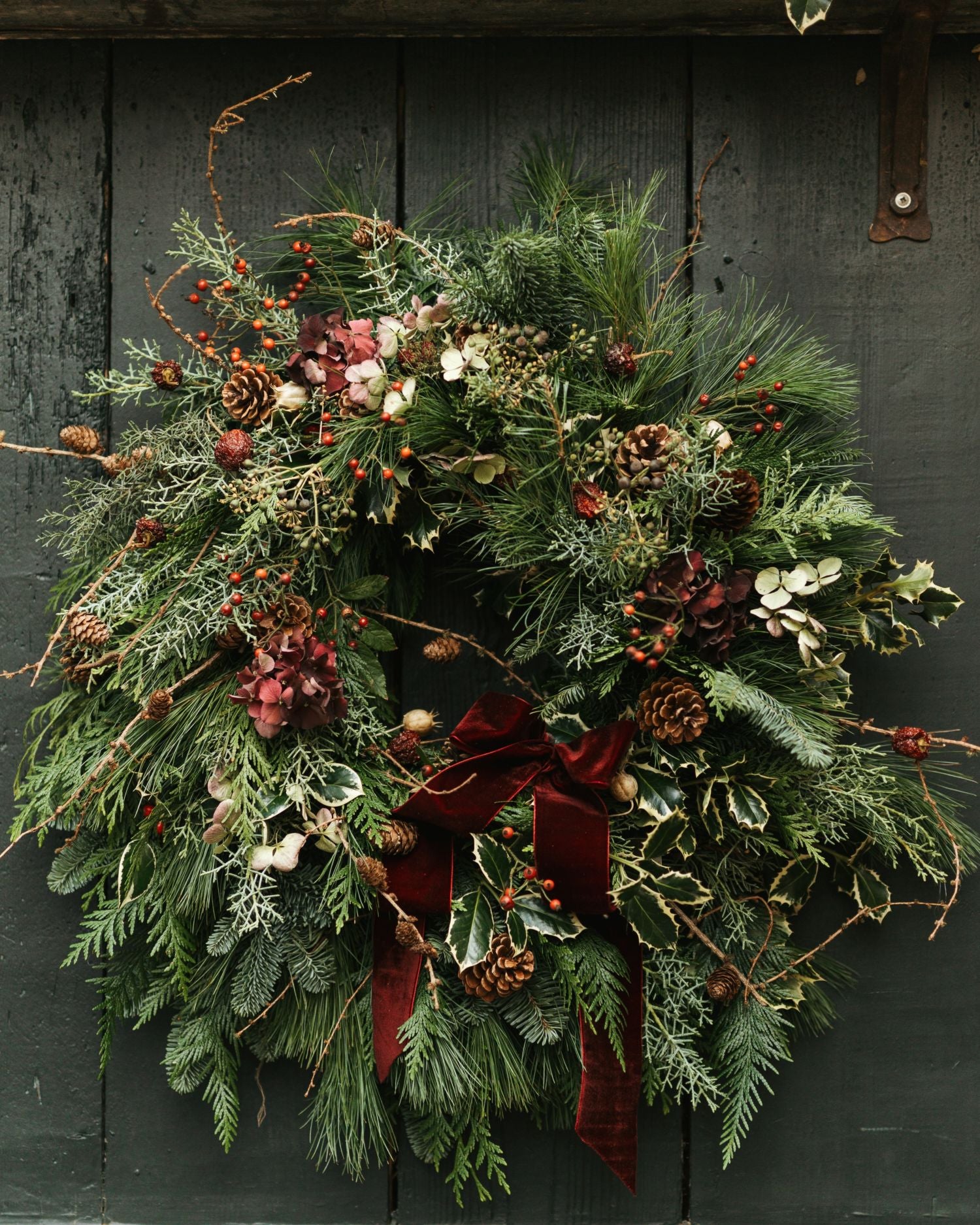 Christmas wreath with greenery, berries, and a red ribbon on a dark wooden background