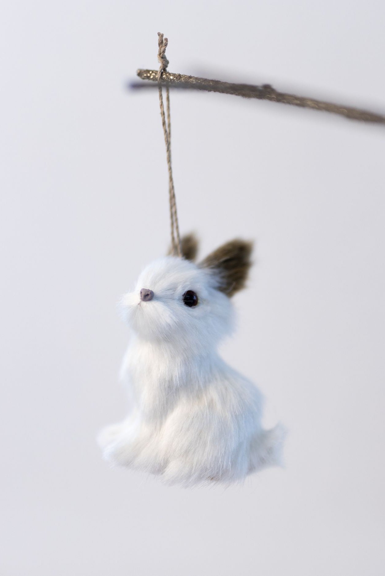 White plush toy rabbit hanging from a branch on a light gray background