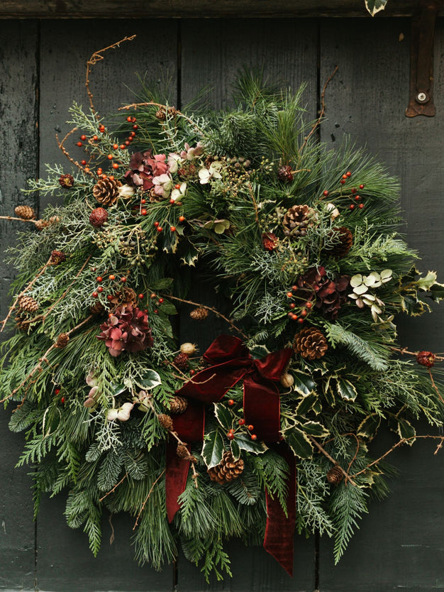 Christmas wreath with greenery, berries, and a red ribbon on a dark wooden background