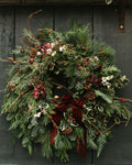 Christmas wreath with greenery, berries, and a red ribbon on a dark wooden background