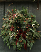 Christmas wreath with greenery, berries, and a red ribbon on a dark wooden background