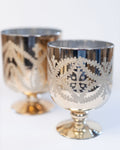 Two silver goblets with intricate designs on a white background