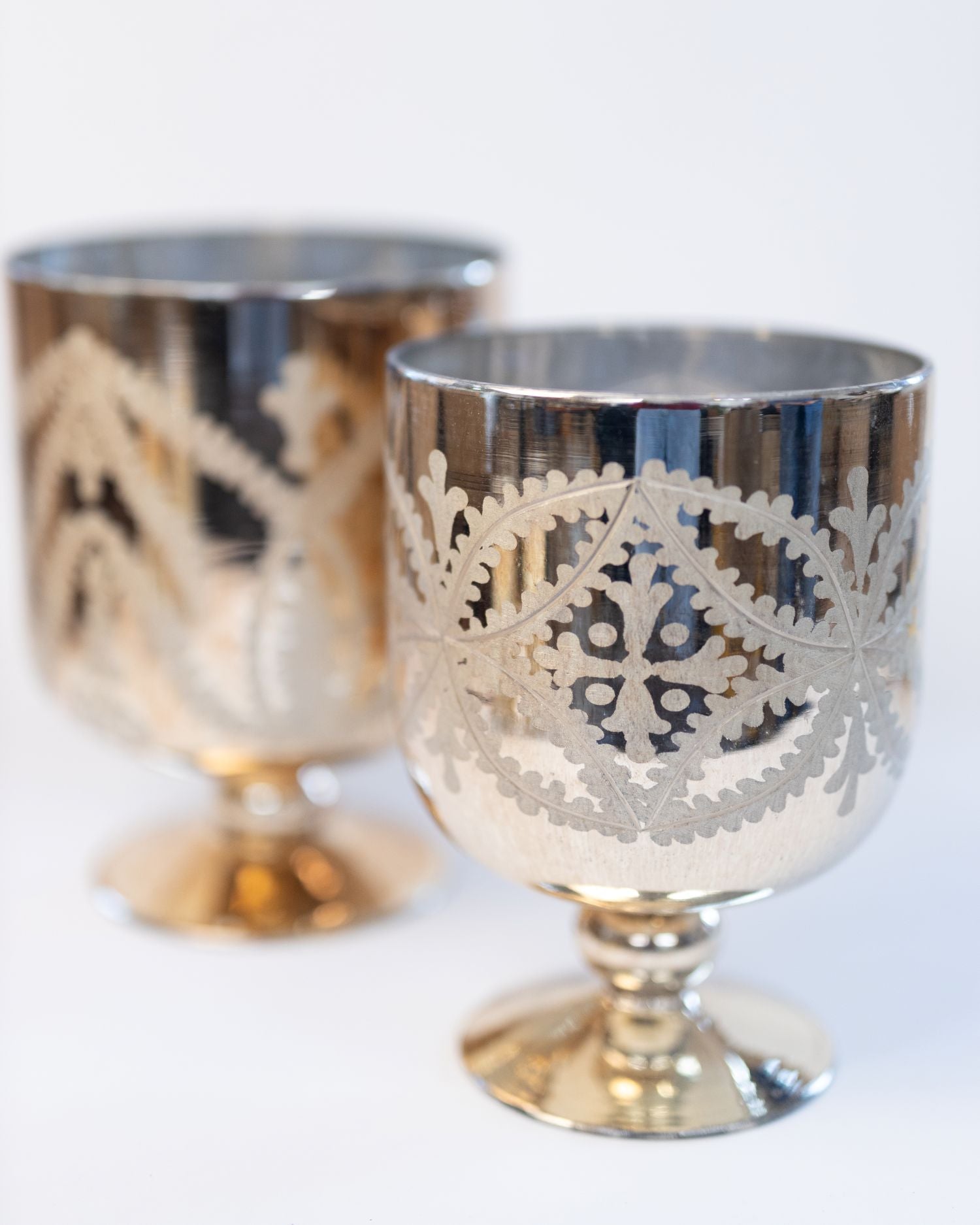 Two silver goblets with intricate designs on a white background