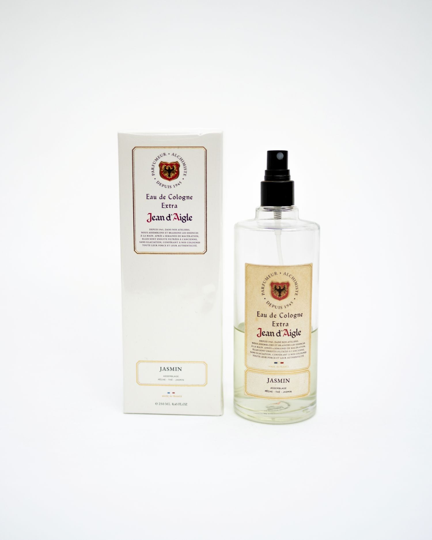 A clear glass perfume bottle with a black spray top stands next to its white rectangular box. Both feature cream labels with a crest and the text 'Jean d'Aigle' and 'Jasmin'.