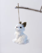 White plush toy rabbit hanging from a branch on a light gray background